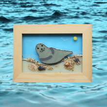 Load image into Gallery viewer, Framed glass artwork of a seal on a beach with ocean waves in the background