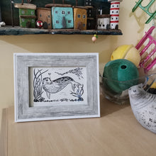 Load image into Gallery viewer, A photograph of a framed linocut of a seal called Arrowhead, made by printmaking artist Holly Dominique, with other items